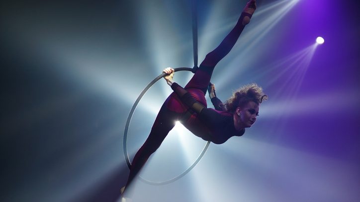 A performer gracefully balances in a hoop, displaying flexibility and strength against a backdrop of dramatic lighting and shadows.