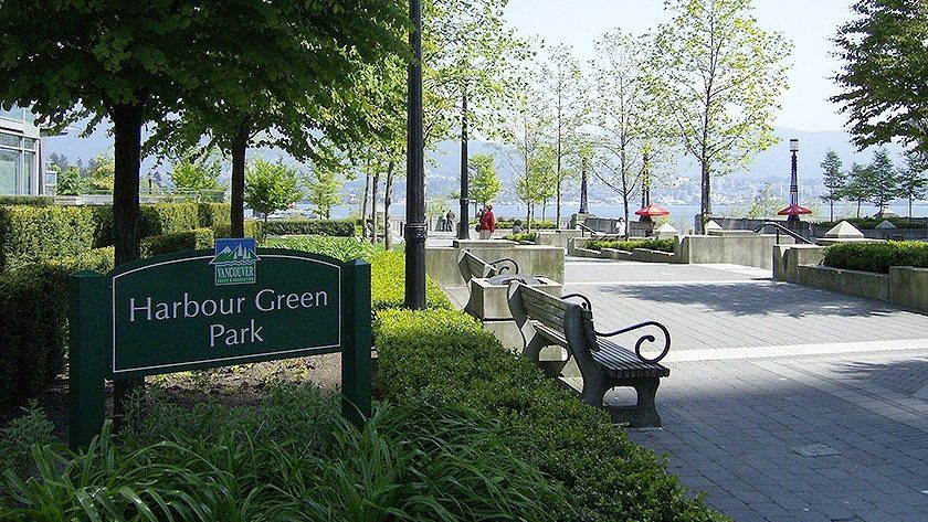 Harbour Green Park sign with landscaped areas, benches, and walking paths, framed by trees overlooking the water in Vancouver.